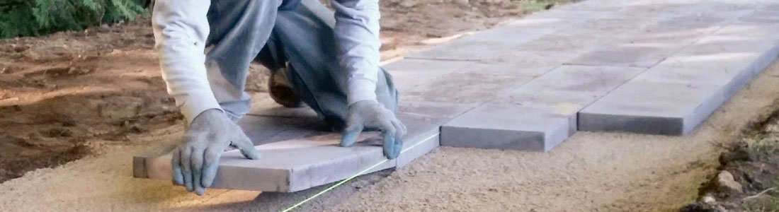 Person laying pavers on a prepared surface during an outdoor creation classes, demonstrating hands-on landscape design techniques.