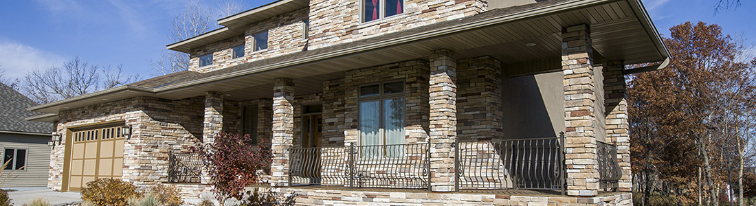 Front view of a modern home with stone veneer facade and large pillars, showcasing natural stone texture and color.